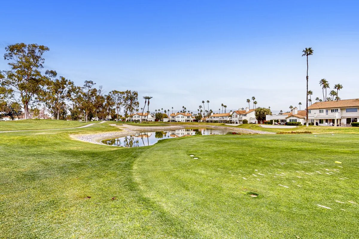A sunny golf course with a pond and palm trees in the distance.