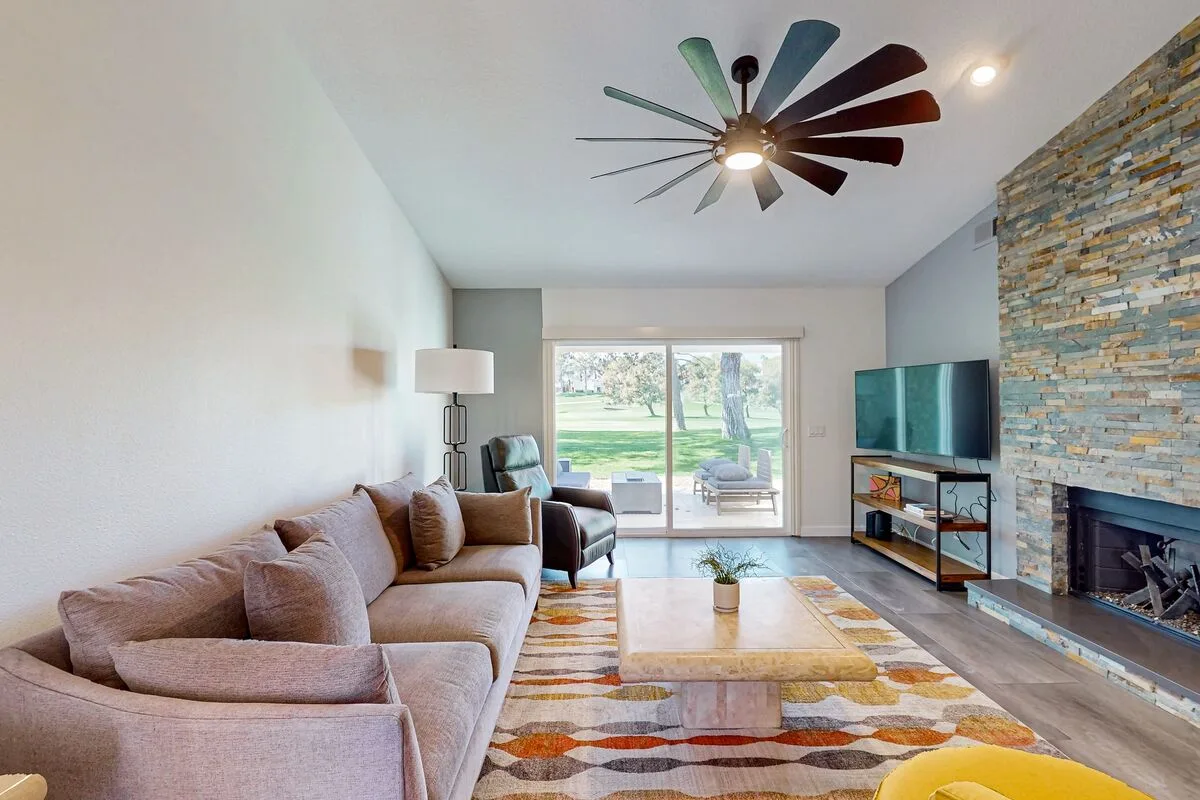 A living room with seating, a fireplace, and windows overlooking a green yard.