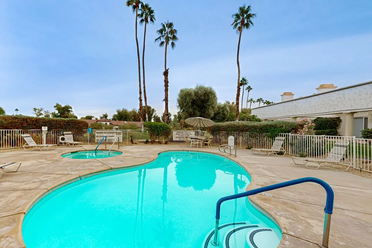 An outdoor swimming pool surrounded by a paved deck and palm trees.