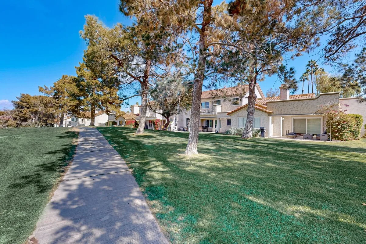 A paved walkway crosses a grassy courtyard in front of residential buildings and trees.