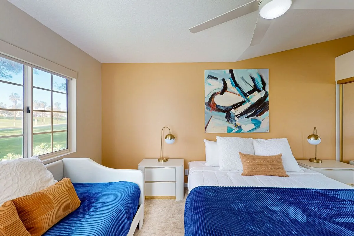 A bedroom with two beds, blue bedding, and abstract artwork above one bed.