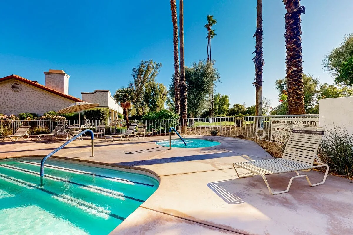 An outdoor pool area with turquoise water, lounge seating, and palm trees.