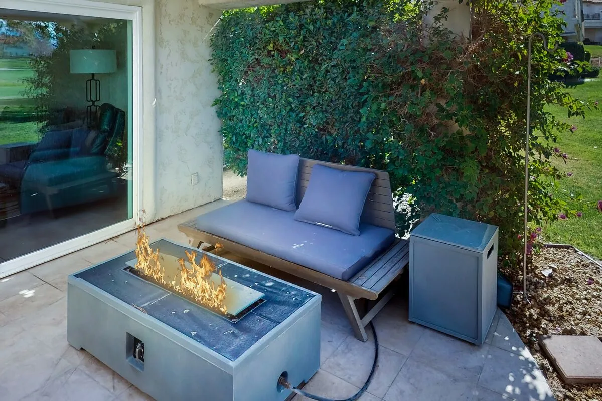 An outdoor patio seating area with a cushioned bench and rectangular fire pit.
