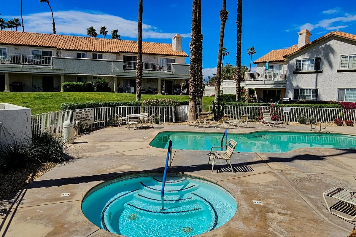 An outdoor pool and circular spa sit in a paved courtyard beside residential buildings.