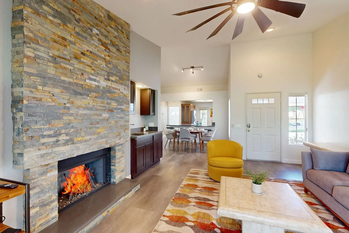A bright living room with a stone fireplace and colorful seating.