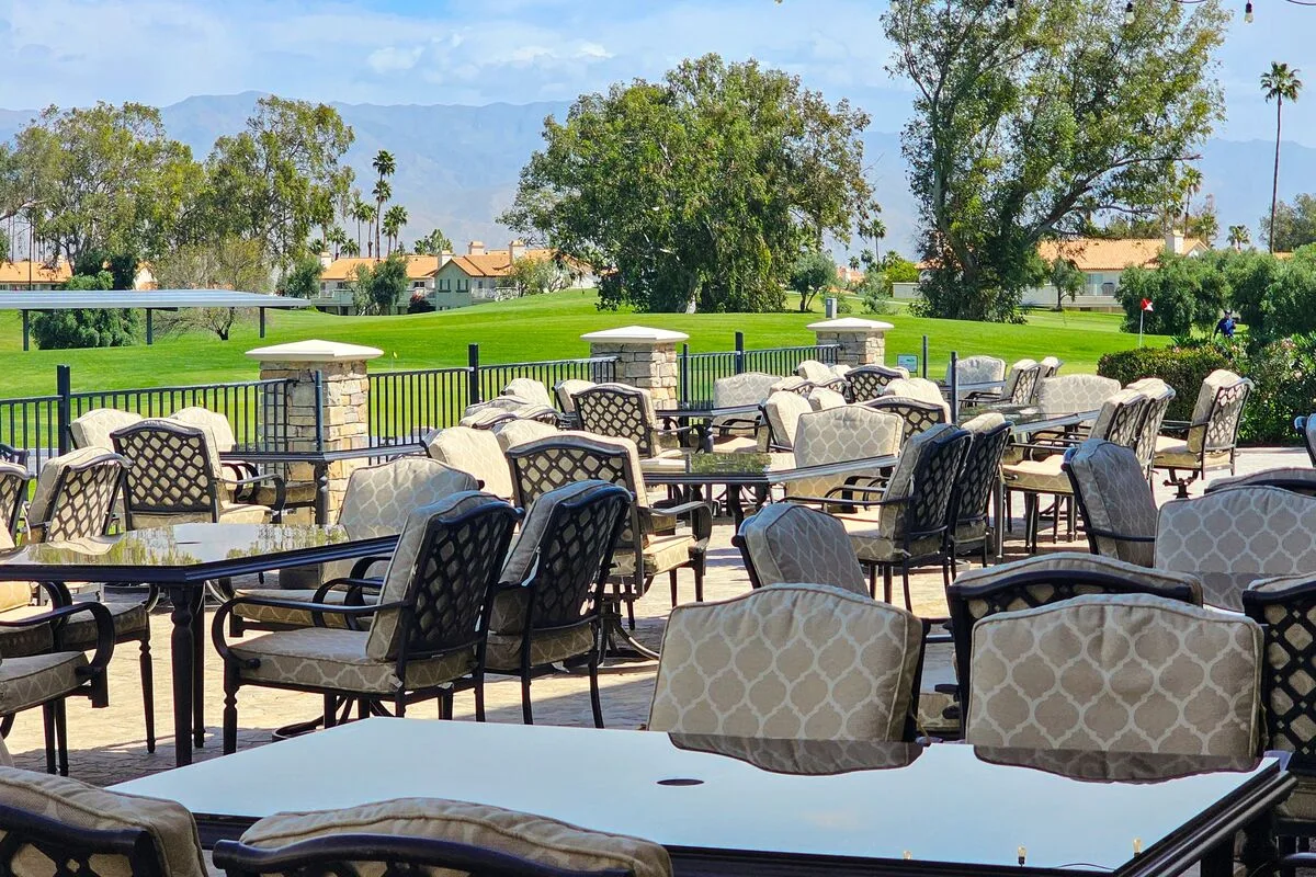 An outdoor dining patio with tables and cushioned seating overlooks a green lawn.