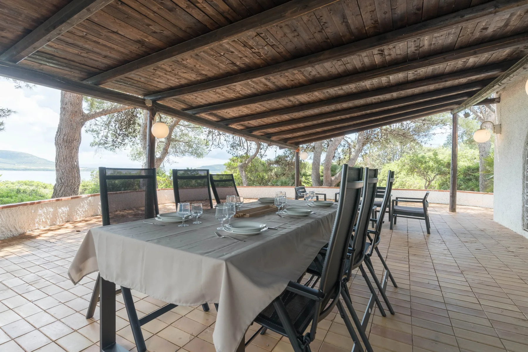 Comedor exterior cubierto con una mesa larga preparada junto a una terraza abierta.