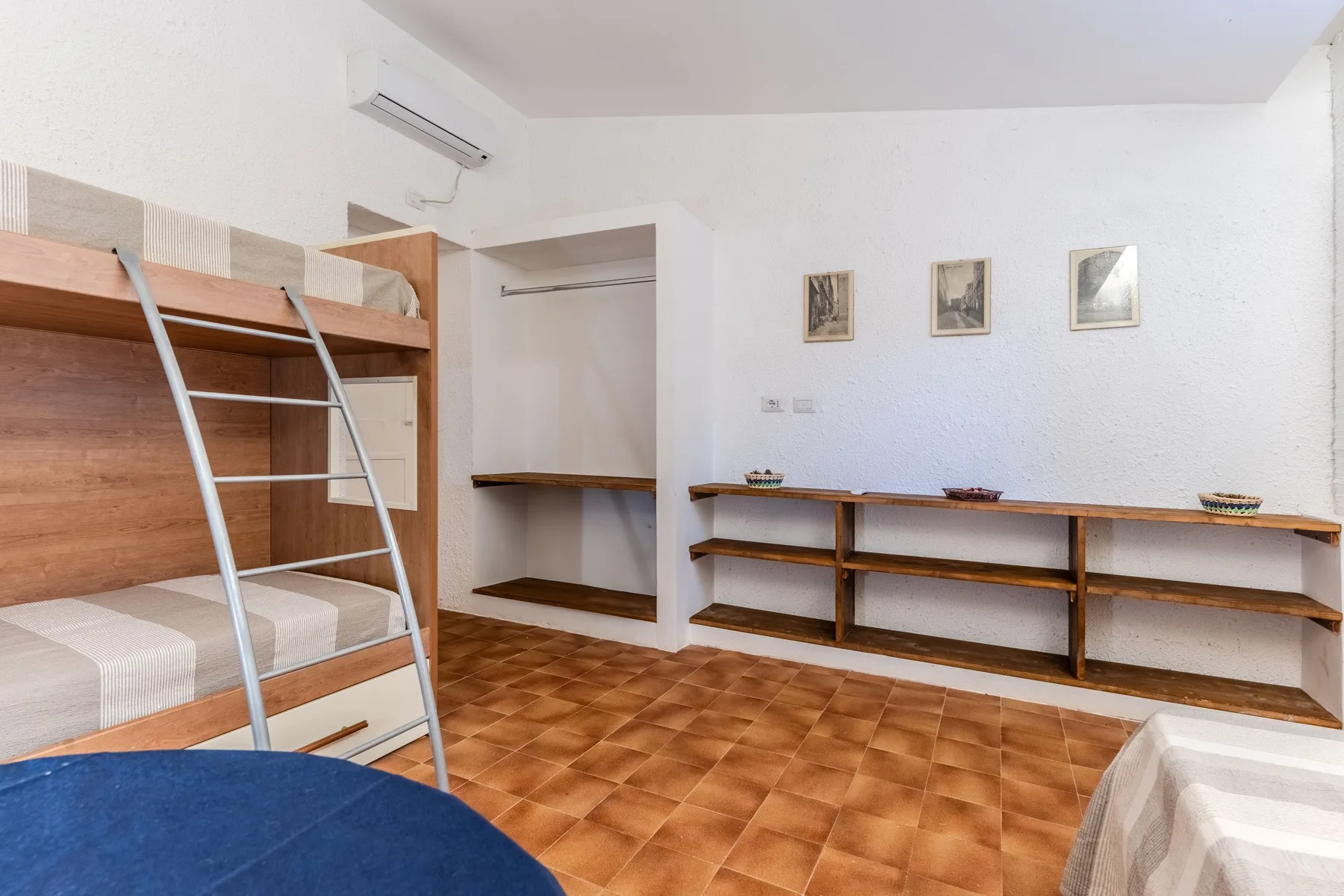 Un dormitorio con una litera de madera, estantes abiertos y suelo de baldosas.
