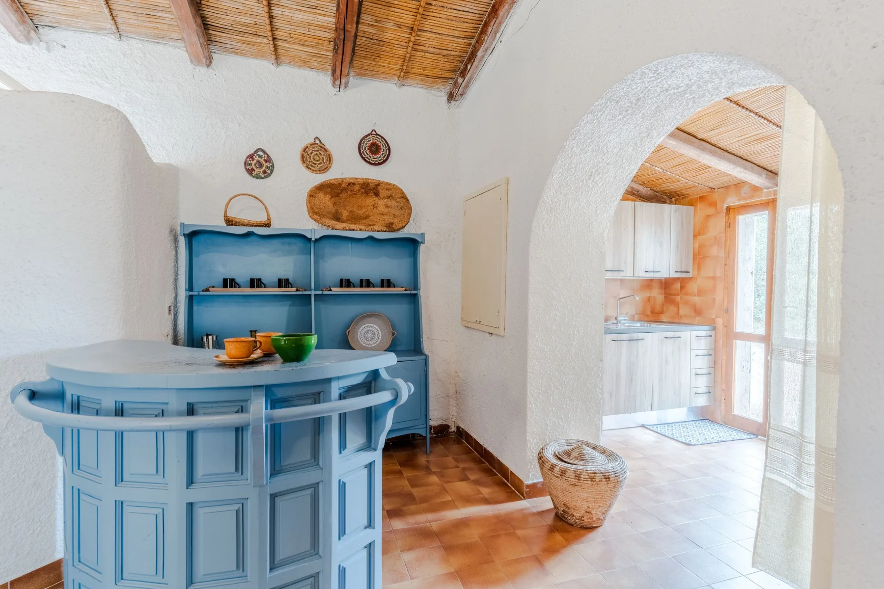 A blue counter and open shelving fill a room with a tiled floor and arched doorway.