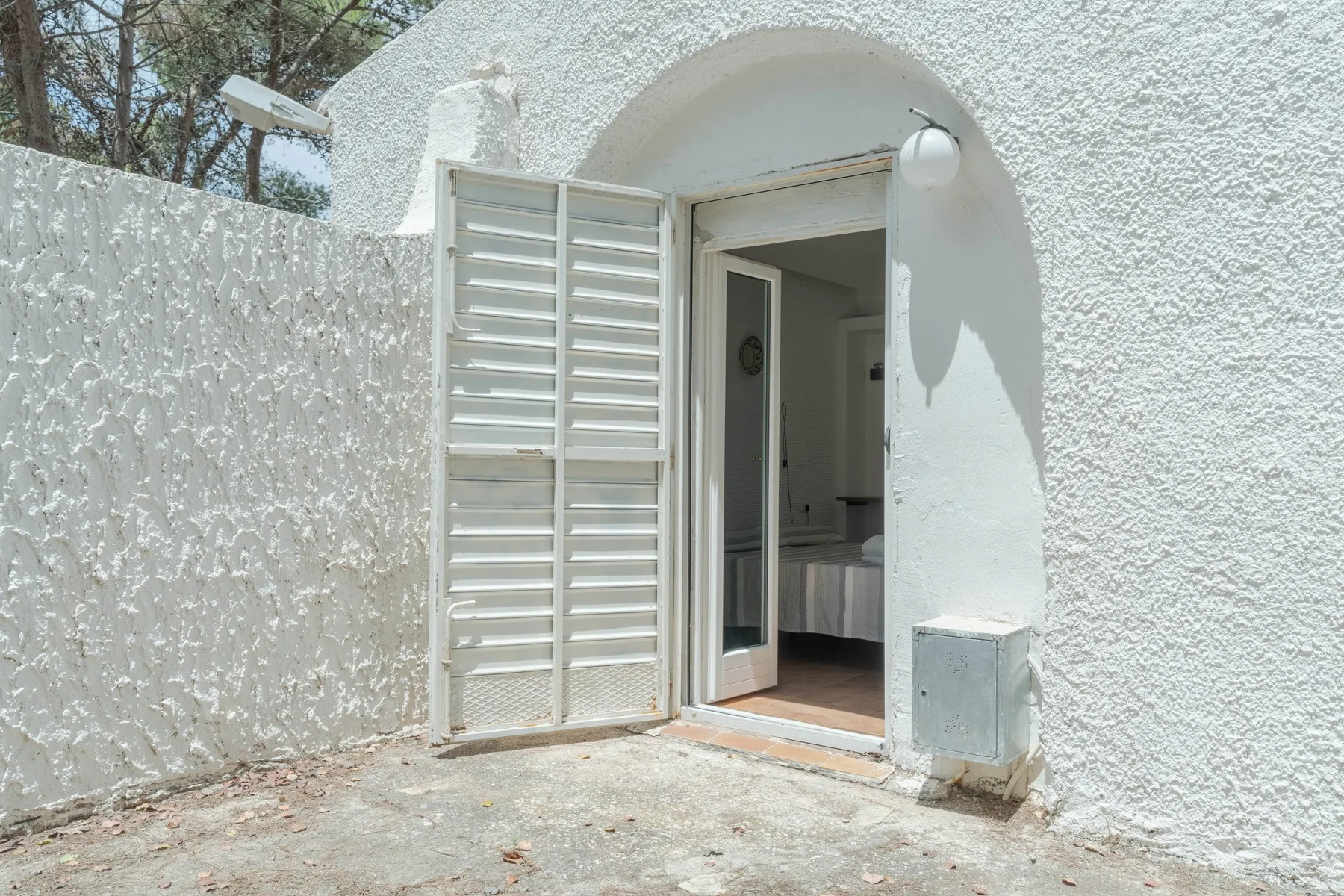 Una entrada blanca con arco se abre a una habitación donde se ve una cama.