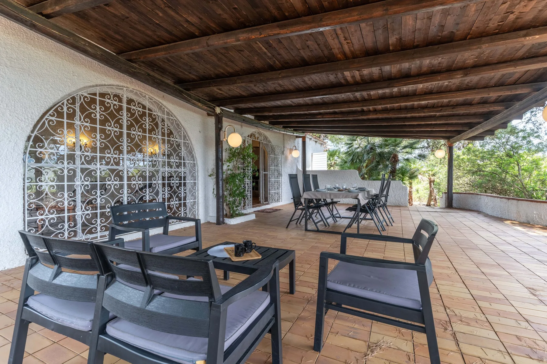 Una terraza exterior cubierta con asientos y una mesa de comedor junto a un jardín.