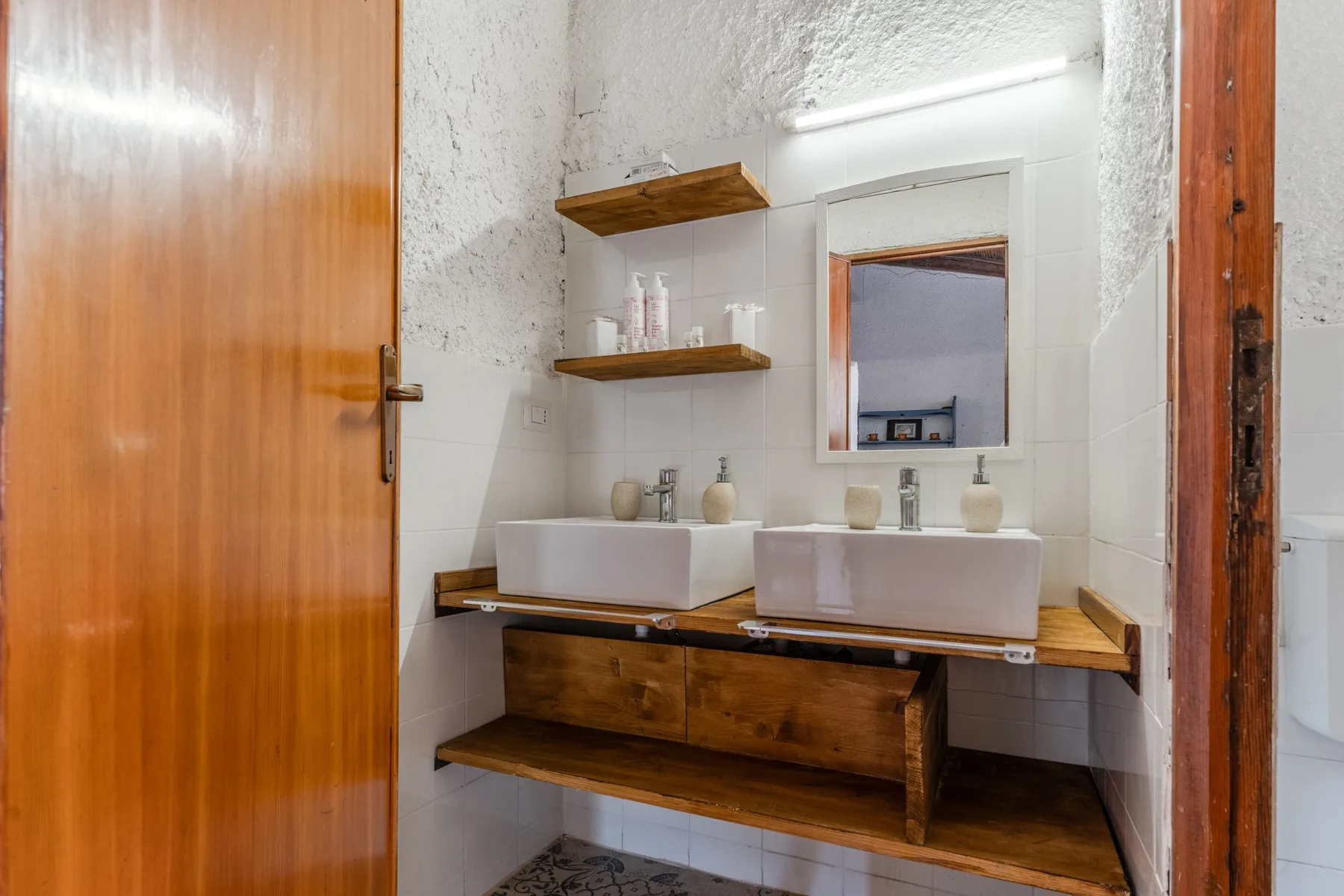 Un tocador de baño con dos lavabos, estantes de madera y un espejo.