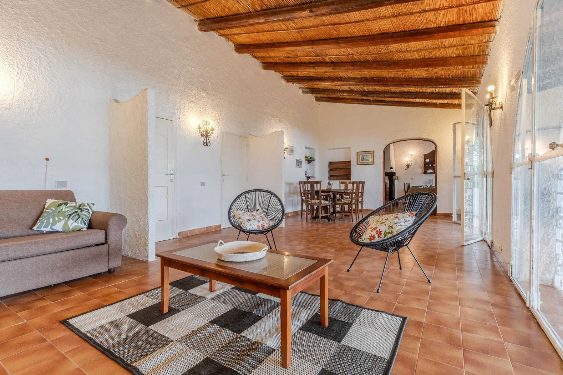 A bright living and dining room with a seating area and wooden ceiling beams.