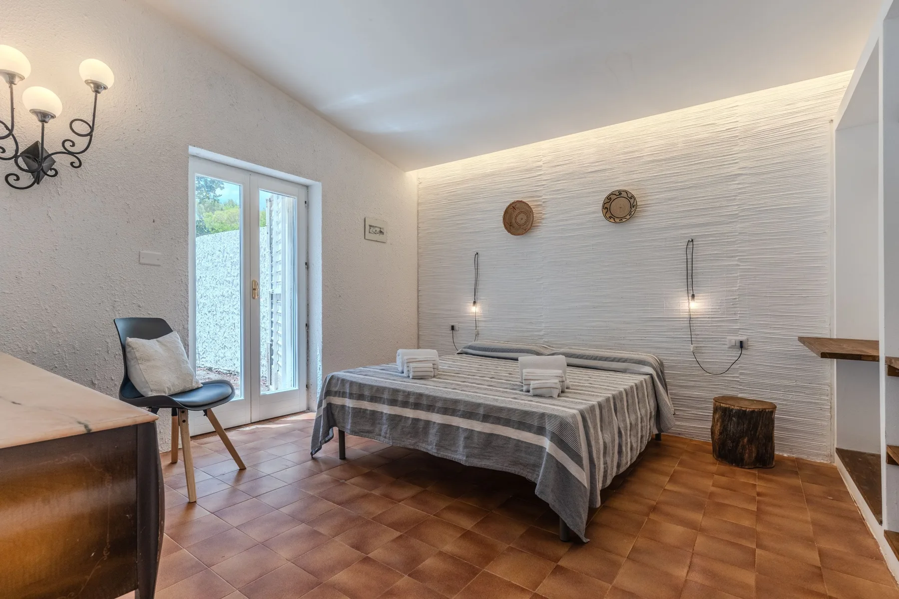 Un dormitorio con una cama doble, luces junto a la cama y una puerta acristalada hacia un balcón.