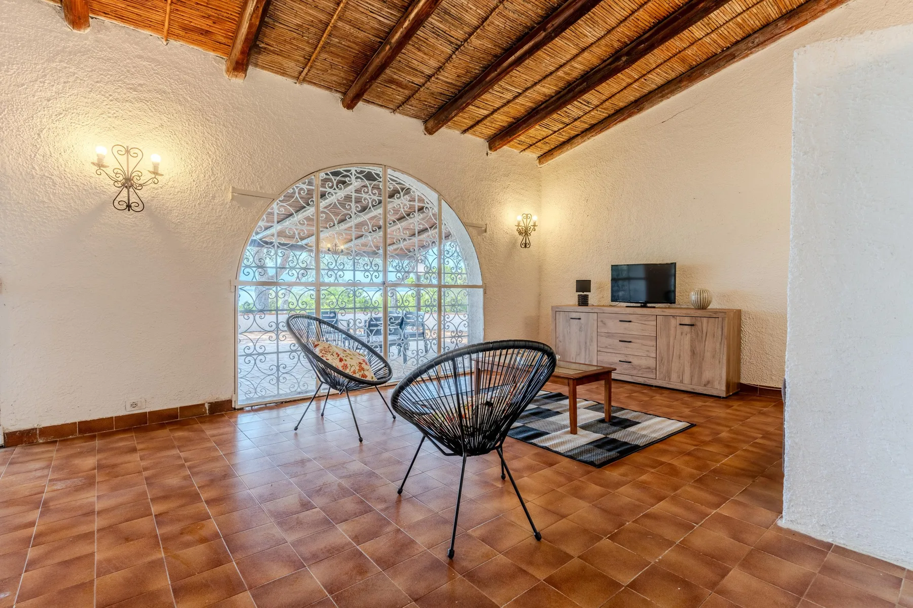 Una sala de estar con asientos, un televisor y una gran ventana arqueada.