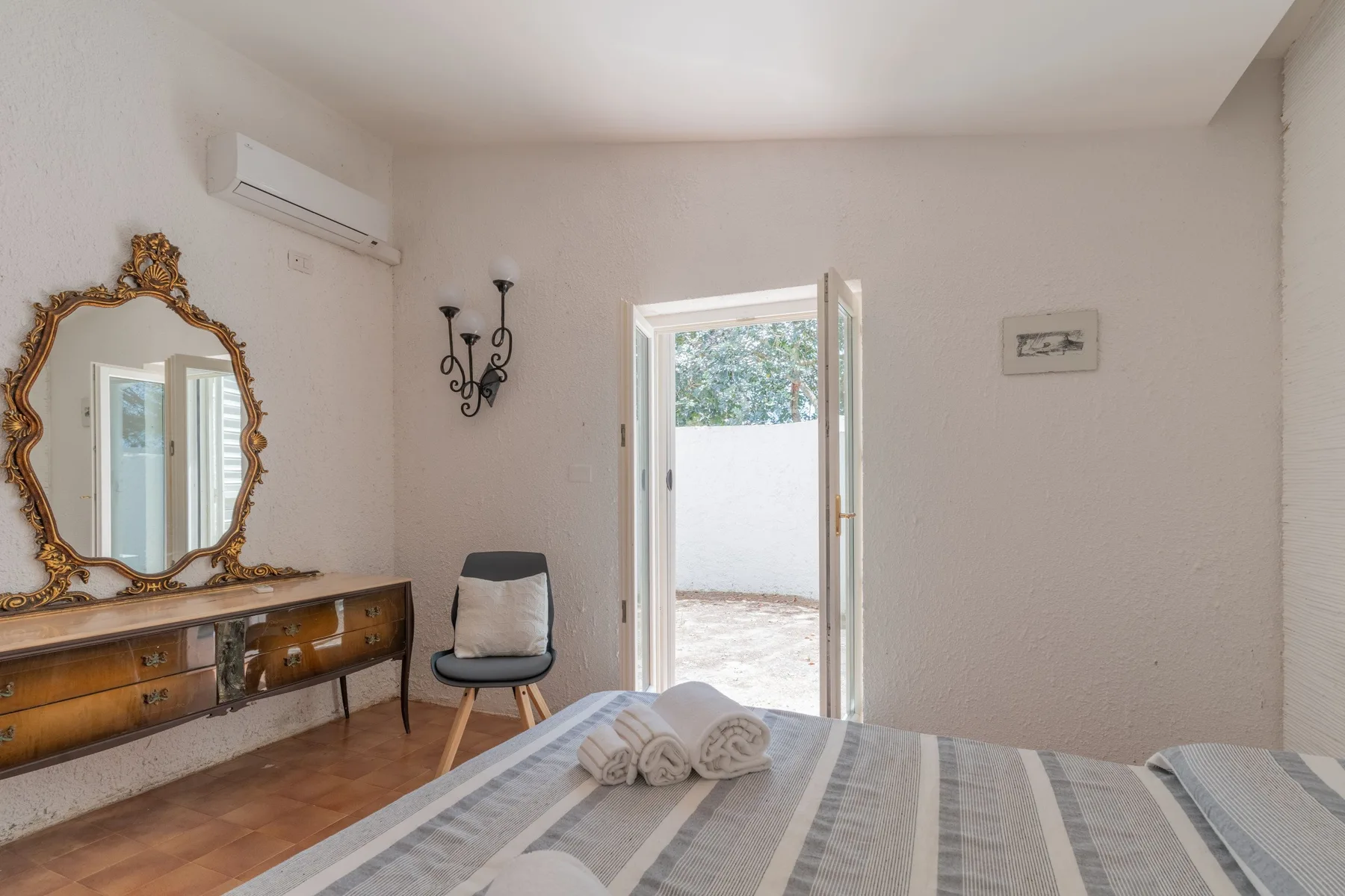Un dormitorio con una cama, una cómoda de madera y una puerta abierta a un patio.