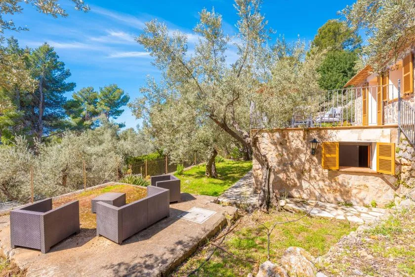 Una casa de piedra da a una zona de estar al aire libre entre árboles.