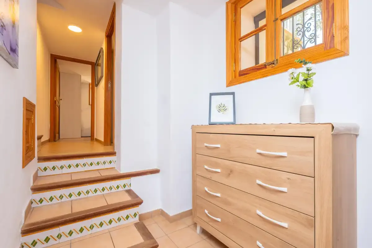 Un pasillo luminoso con escalones de azulejos y una cómoda de madera.