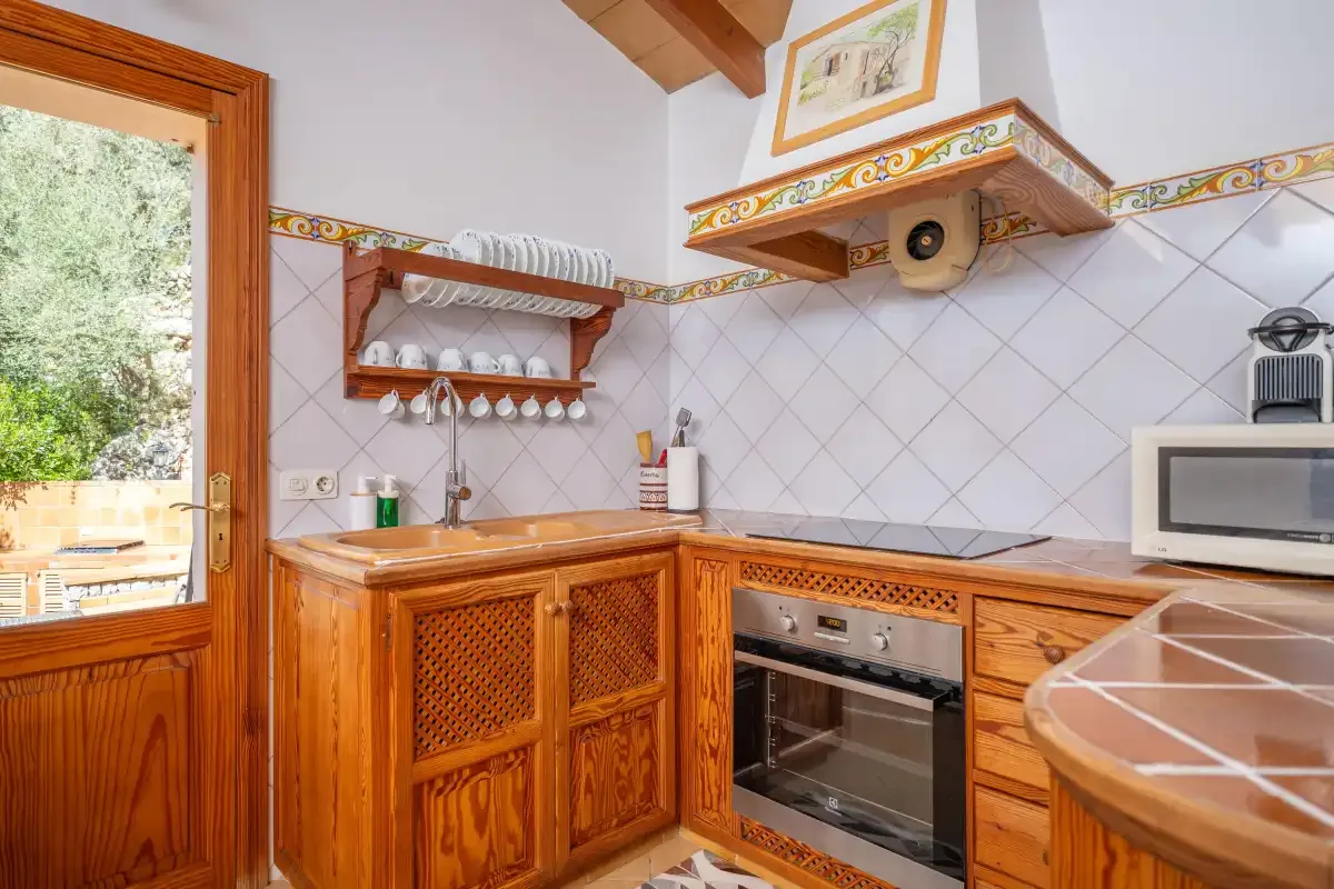 Una cocina alicatada con armarios de madera, horno y una ventana con vistas a la vegetación.