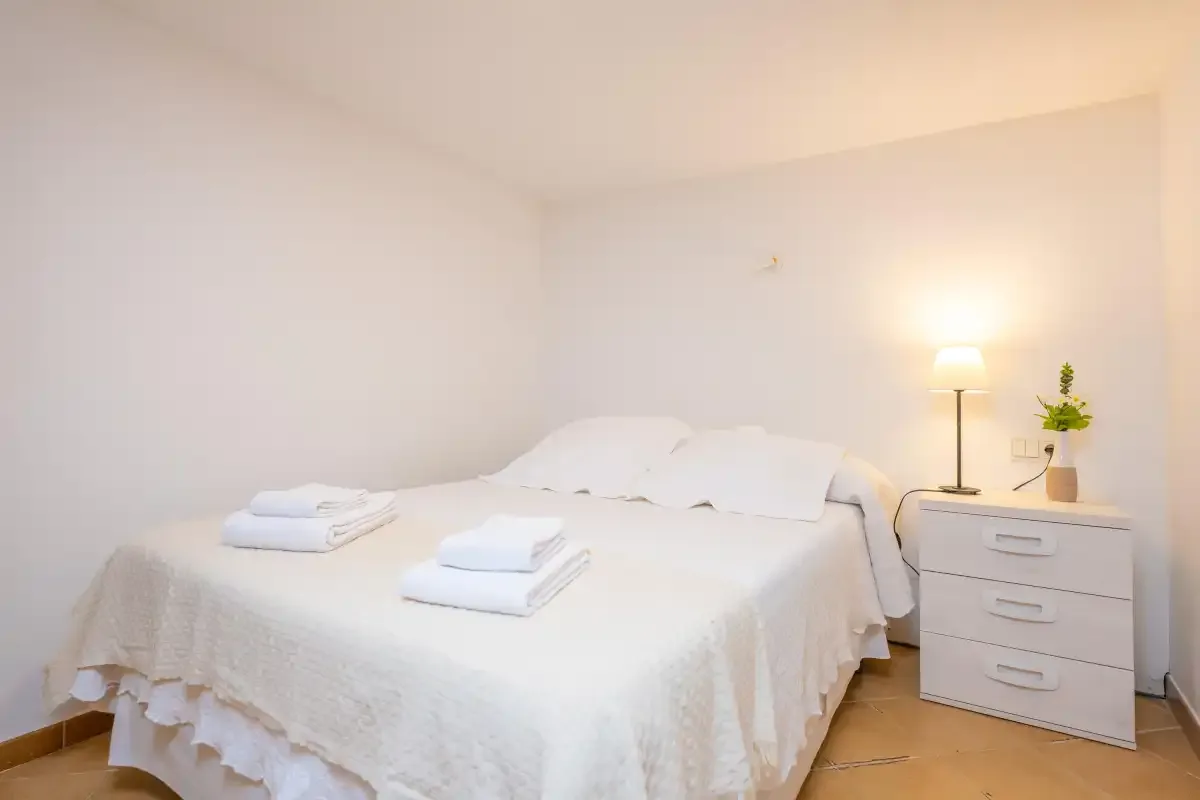 Un dormitorio luminoso con una cama blanca y una mesita de noche.