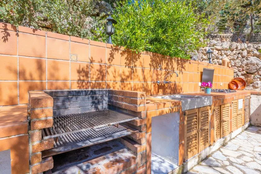 Una zona de cocina al aire libre con una parrilla empotrada y una encimera de azulejos.