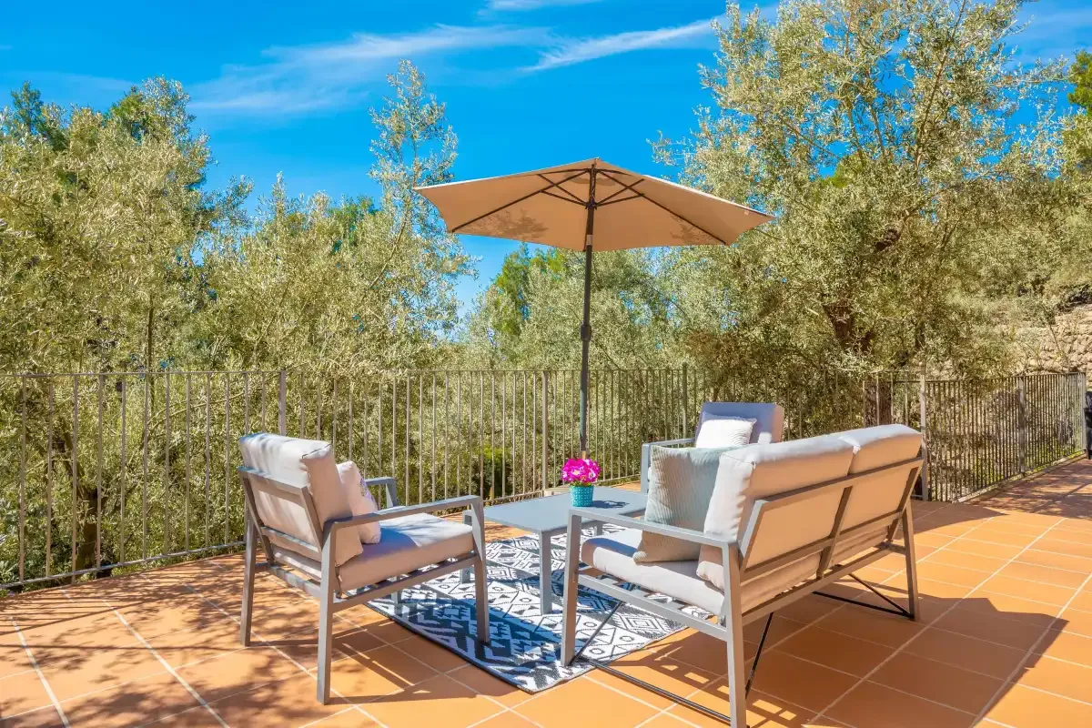 Una zona de estar en un patio exterior, con mesa y sombrilla, da a árboles frondosos.