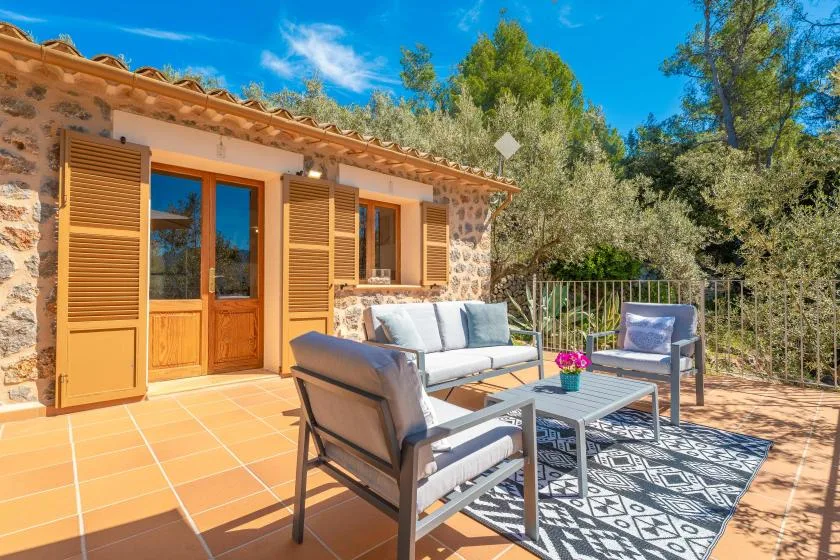 Un patio exterior con asientos y una alfombra estampada junto a una casa de piedra.