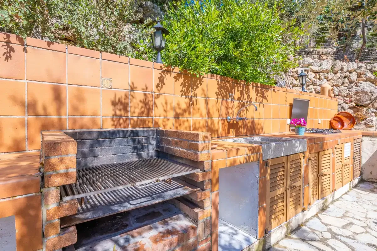 Una cocina exterior con una parrilla empotrada y una encimera de azulejos.