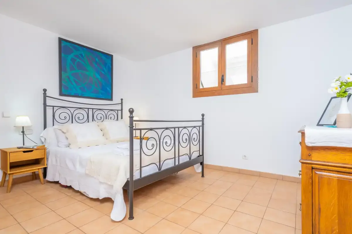 Un dormitorio con una cama de metal, ropa de cama blanca y una ventana de madera.