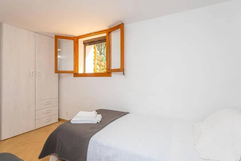 Un dormitorio luminoso con una cama junto a una ventana de madera abierta.
