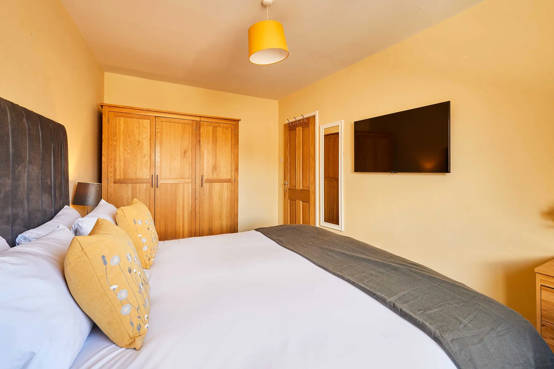 Dormitorio con cama, armario de madera y televisor en la pared.
