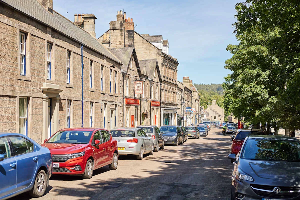 Una calle soleada bordeada de edificios de piedra y coches estacionados.