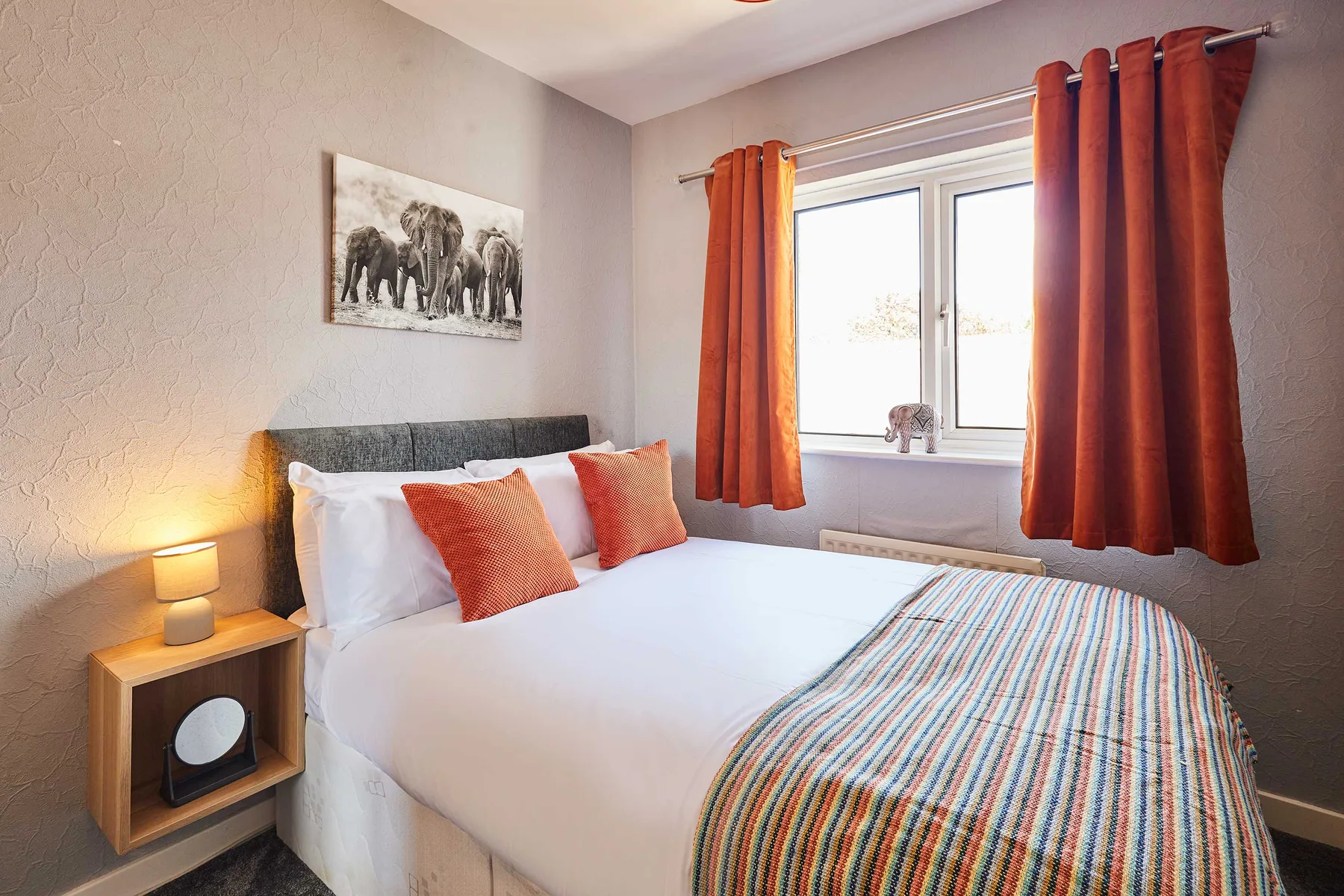 Un dormitorio con una cama bien tendida y cortinas naranjas junto a la ventana.