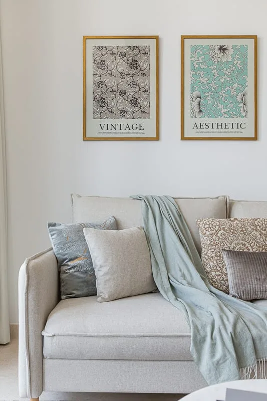 A light-colored sofa with cushions and a draped throw sits beneath two framed prints.