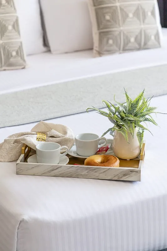 A bed with a tray holding cups, pastries, and a potted plant.