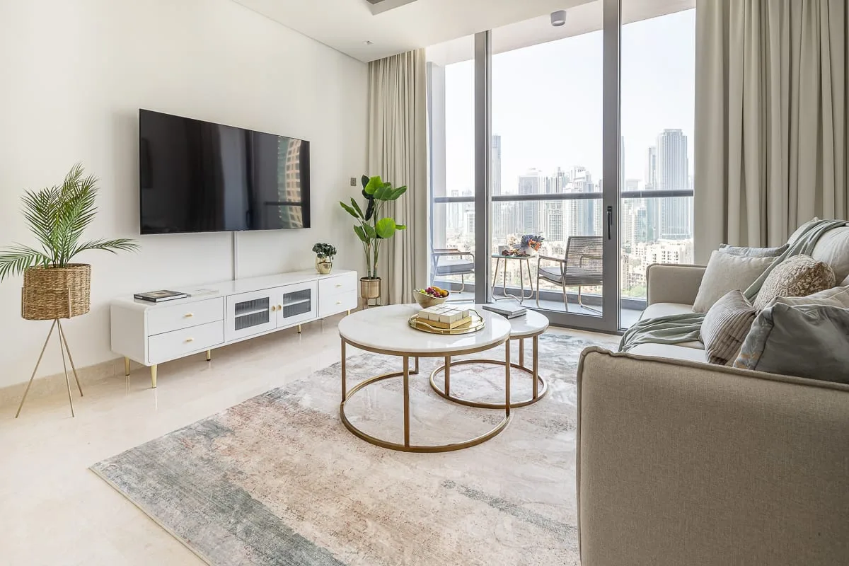 Una sala de estar luminosa con televisor, asientos y grandes ventanales con vistas a la ciudad.