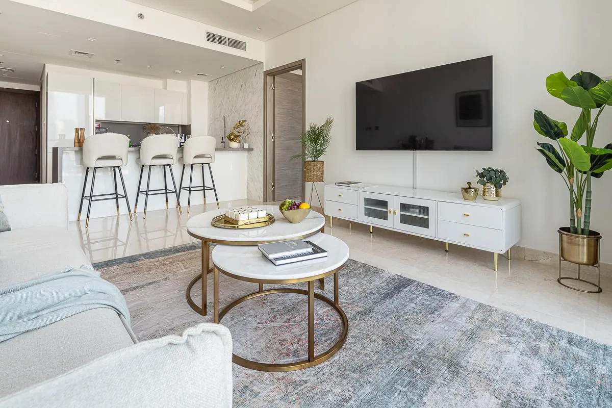 A bright living room with a television, seating, and an open kitchen area.