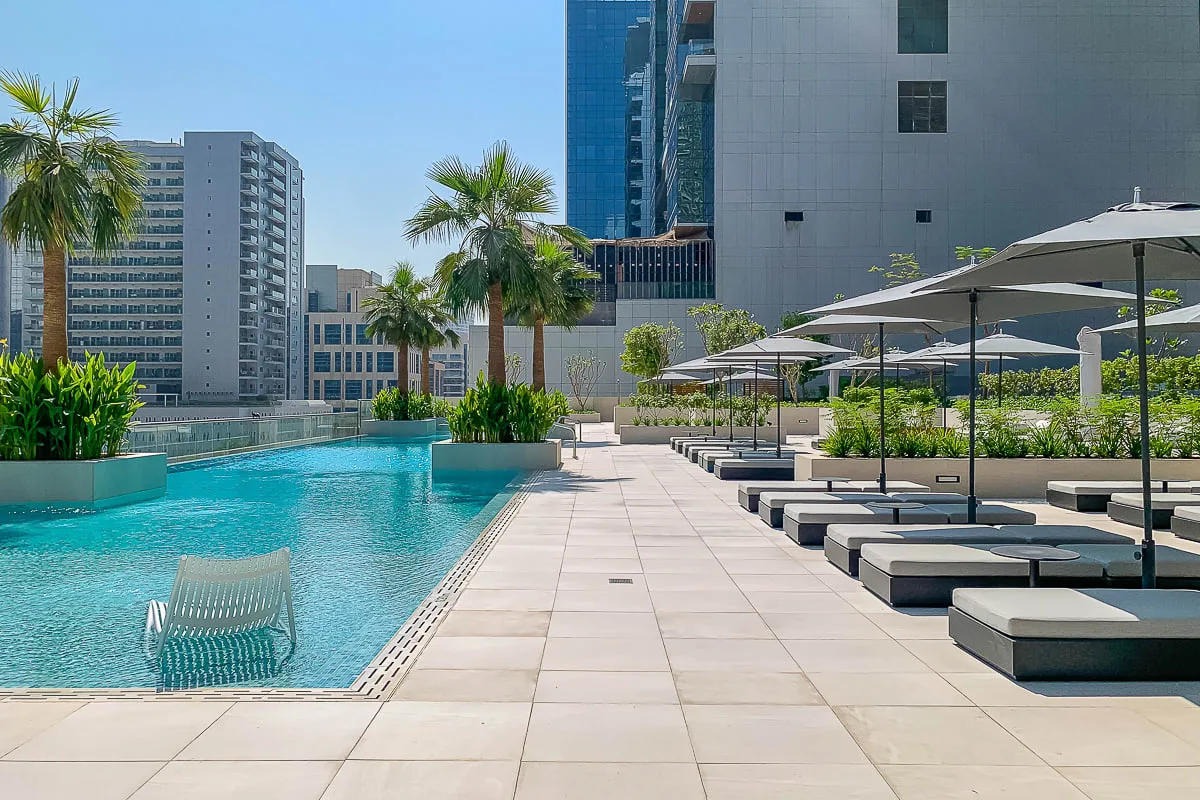 An outdoor pool beside a paved deck with loungers and umbrellas.
