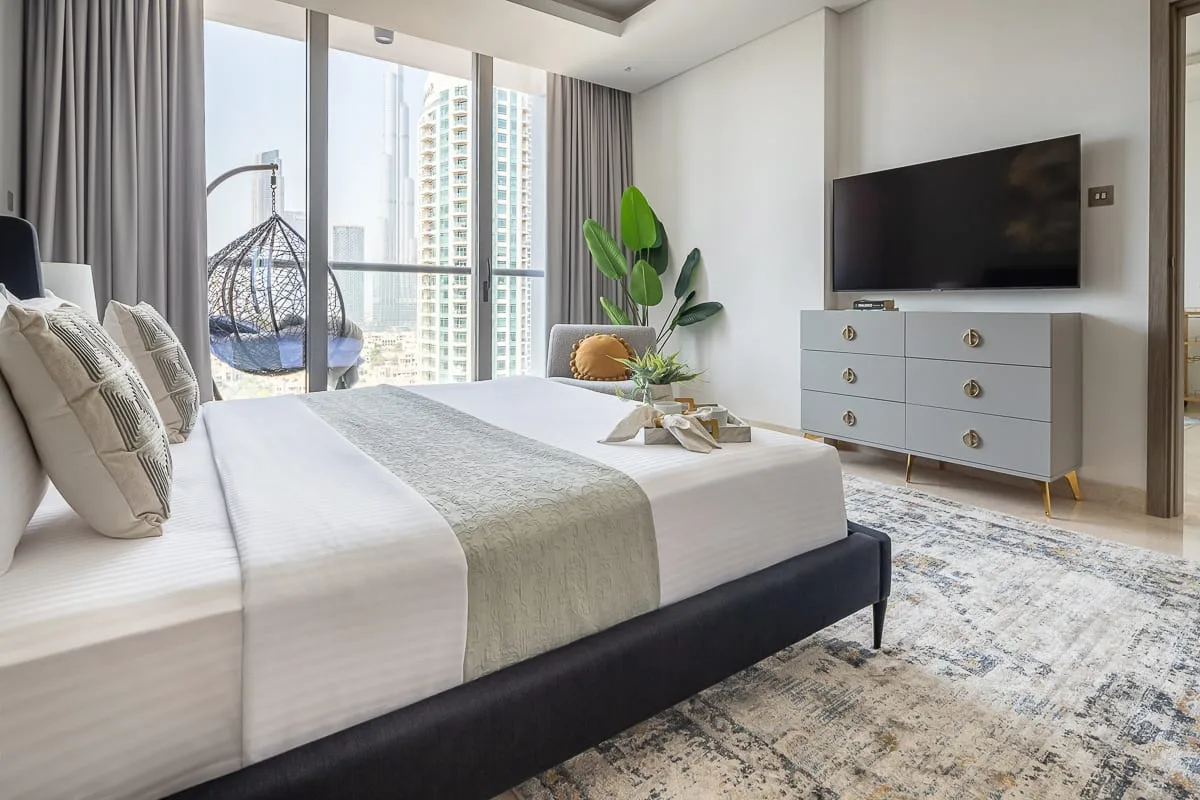 Un dormitorio luminoso con una cama bien tendida y un televisor sobre una cómoda.