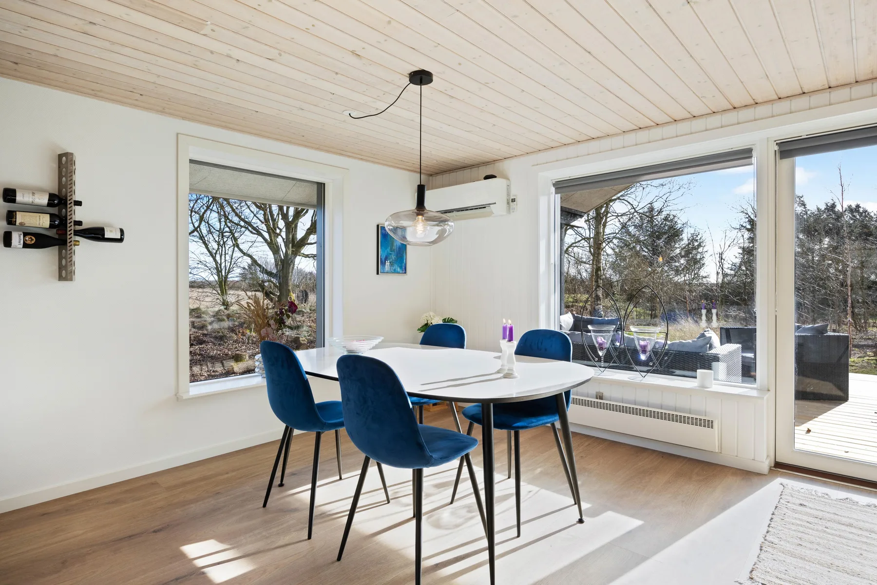 Un comedor luminoso con una mesa y asientos azules junto a grandes ventanales.