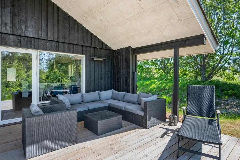 Una terraza exterior tiene una zona de asientos y una silla reclinable junto a una pared de madera oscura.