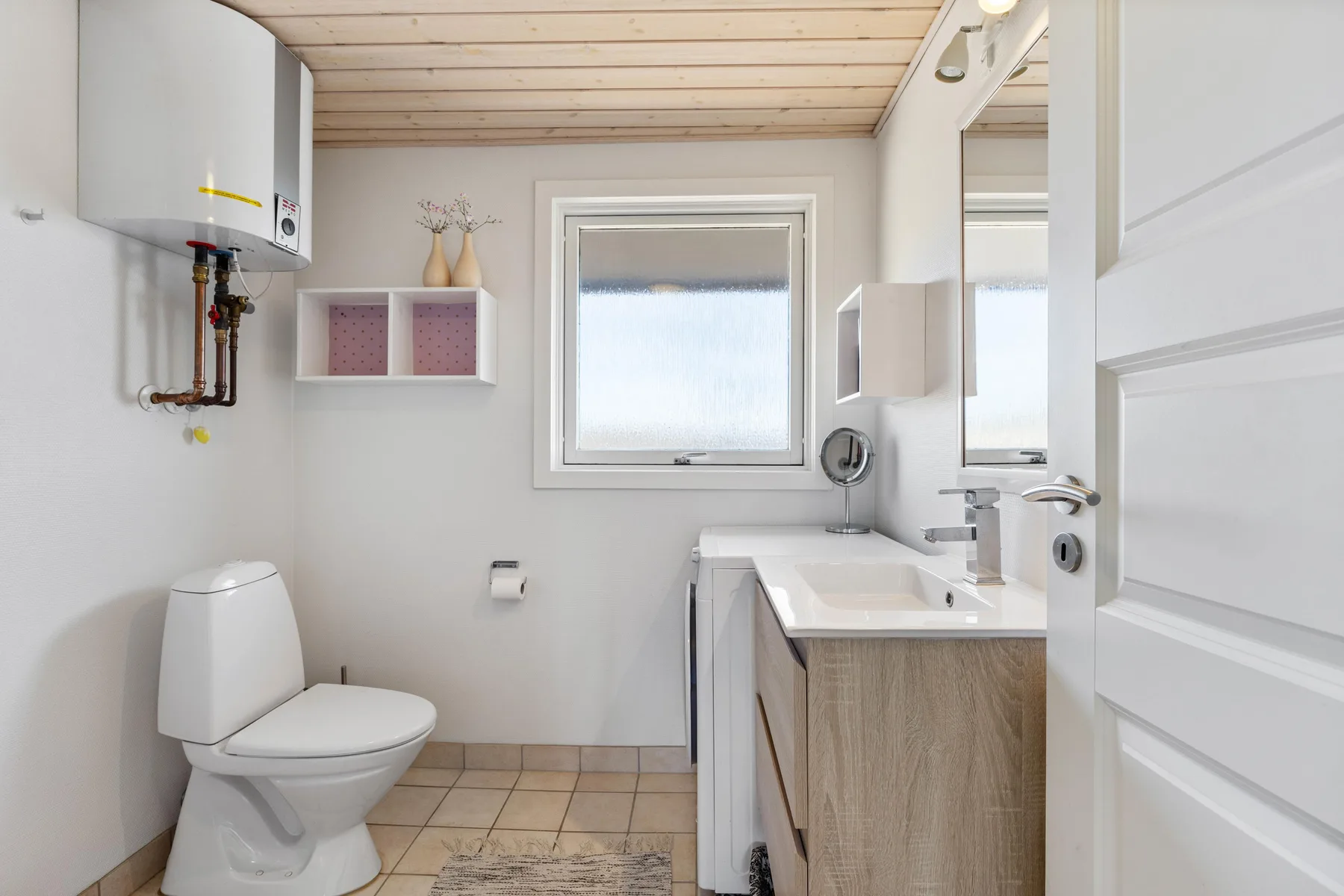 Un baño luminoso con inodoro, mueble con lavabo y ventana.