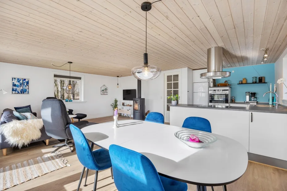Una cocina abierta al comedor, con una mesa blanca y asientos azules.