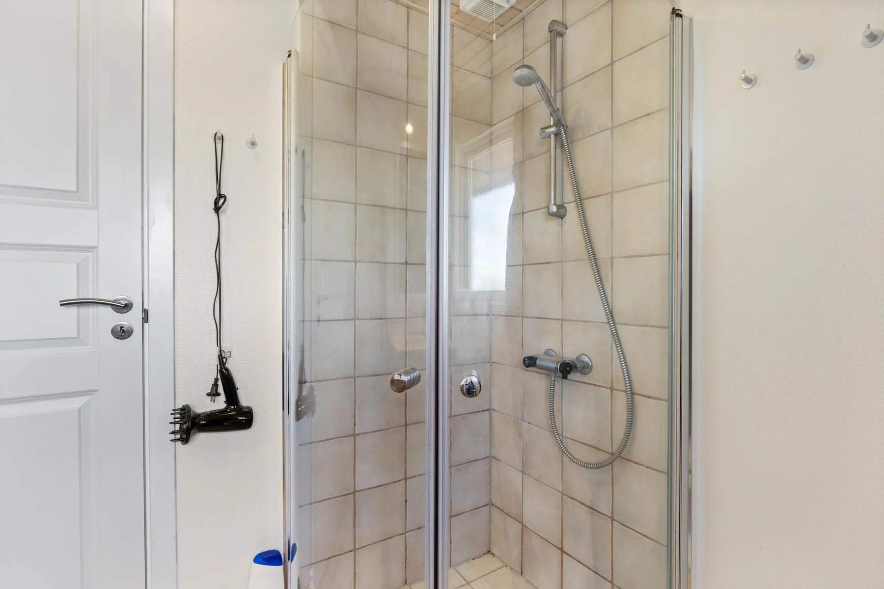 Una ducha con azulejos, paneles de vidrio y una alcachofa montada en la pared.
