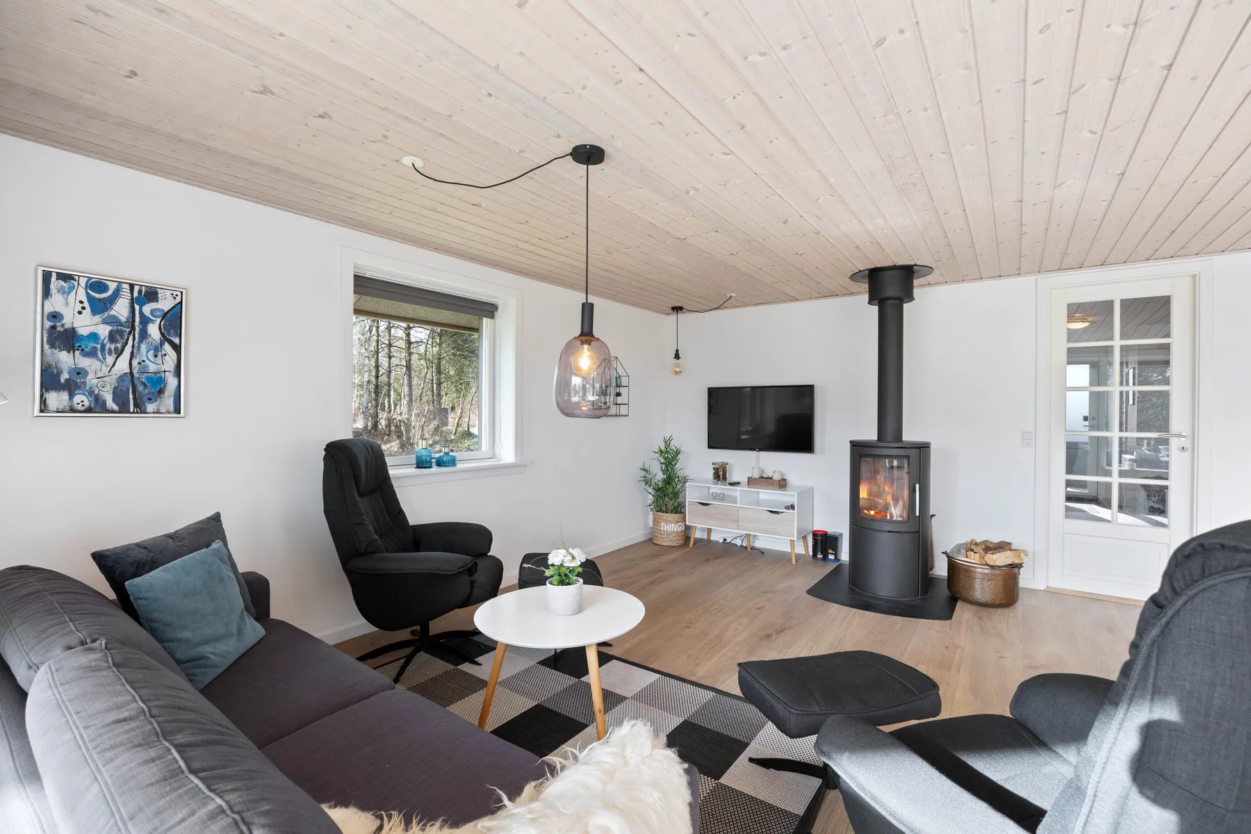 Una sala de estar luminosa con techo de madera, asientos y una estufa independiente.
