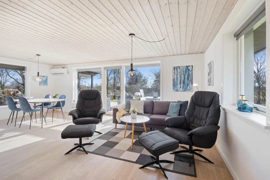 Una sala de estar luminosa con sofá y sillones junto a grandes ventanas.