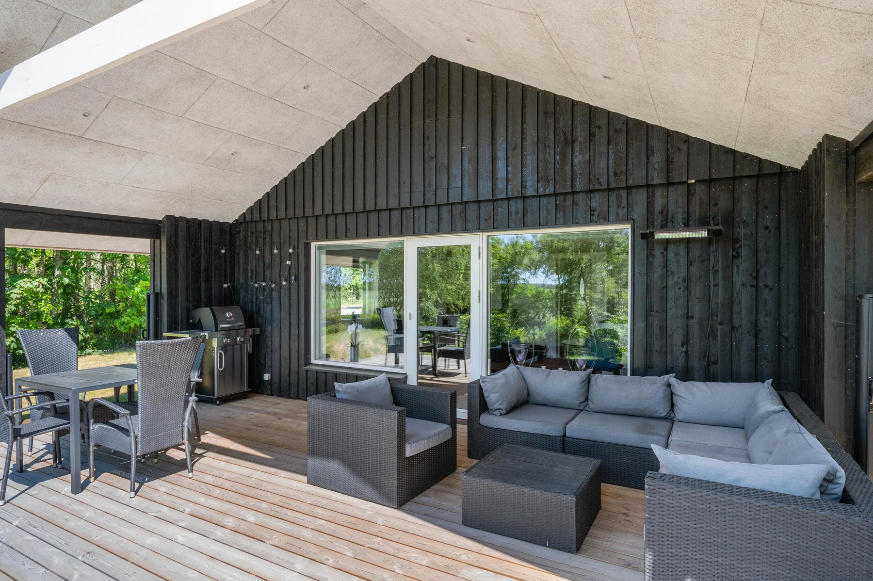 Un patio cubierto con asientos de exterior y puertas de vidrio que dan a un jardín.