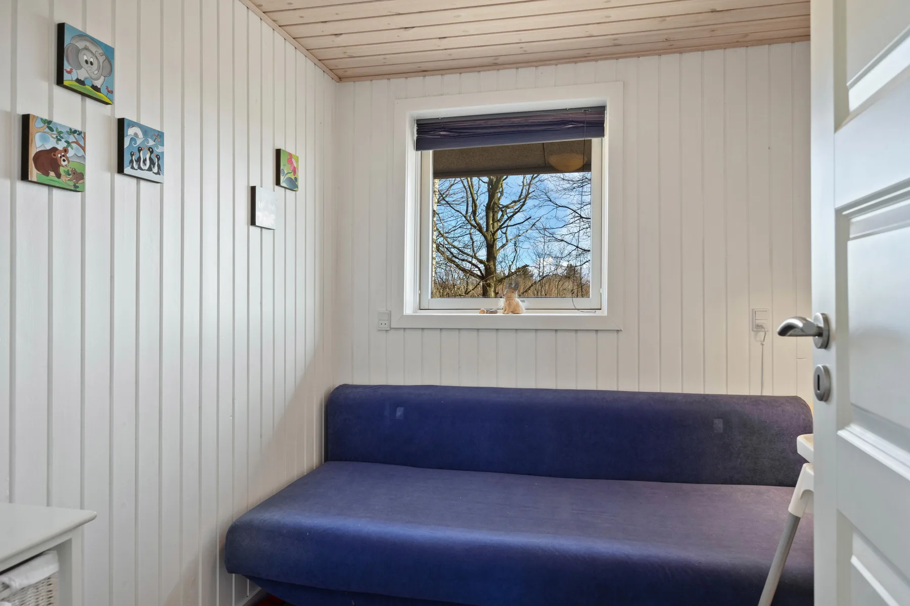 Una habitación pequeña con un banco tapizado azul debajo de una ventana.
