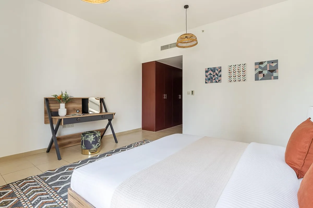 A bright bedroom with a neatly made bed and a small desk.