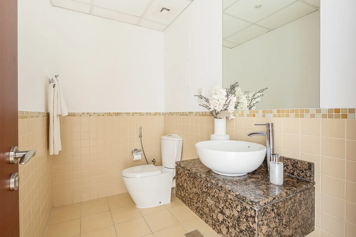 A tiled bathroom with a toilet and a vessel sink on a stone vanity.